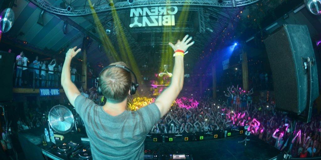 calvin-harris-amnesia-ibiza-openverse Male Dj with hands in the air dancing out to a full crowd. Colourful strobe lights shining down into crowd.