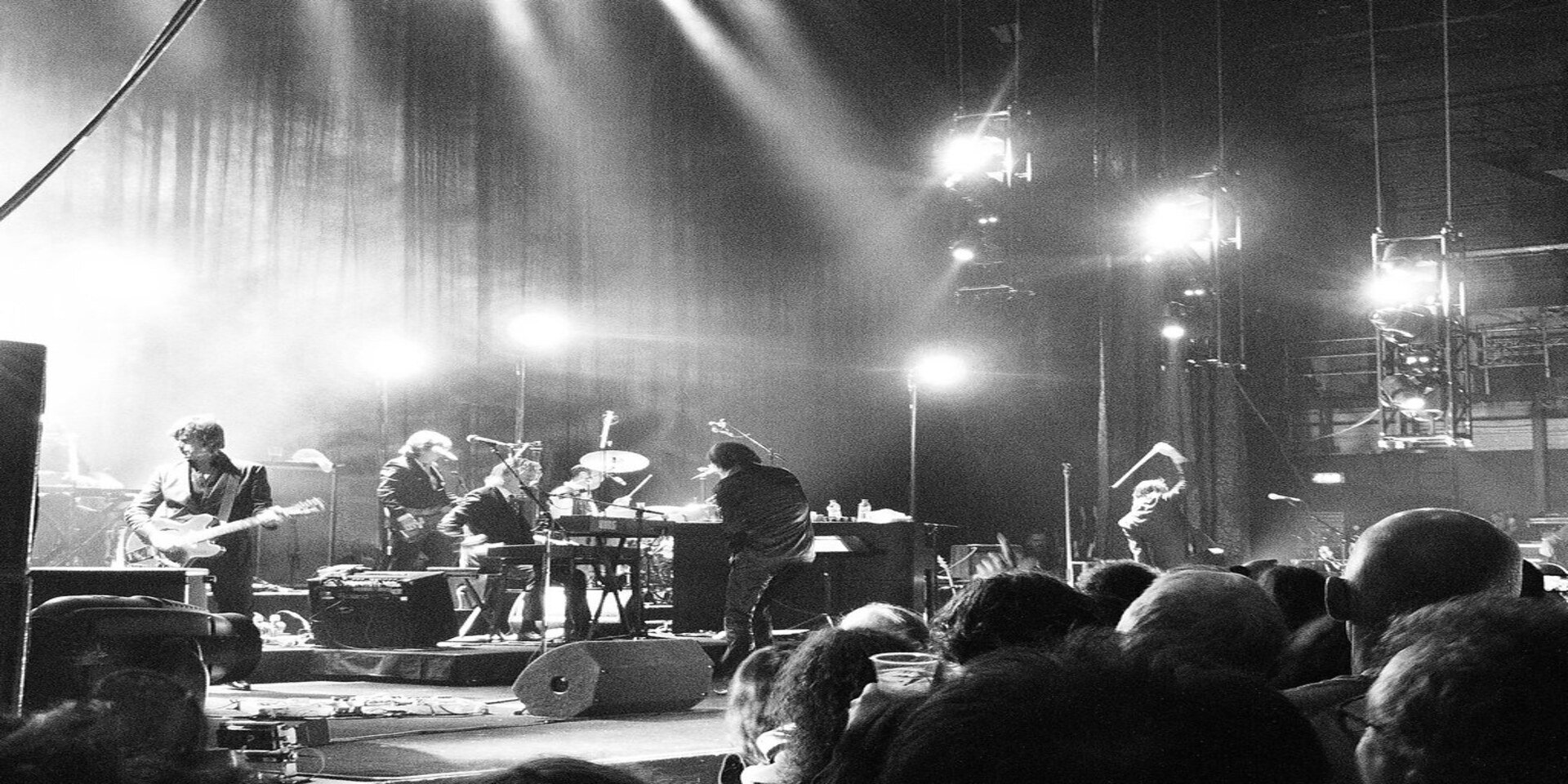 nick-cave-and-the-bad-seeds-paulcarless Black and white image of Nick Cave and The Bad Seeds band on stage during their indoor concert with people dancing in crowded venue and bright flashing lights shining during concert