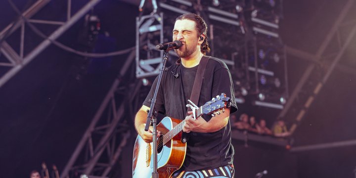 Noah Kahan at Glastonbury Festival 2025 07 by Raph PH is licensed under CC BY 4 0 resized man singing into mic while holding guitar on stage