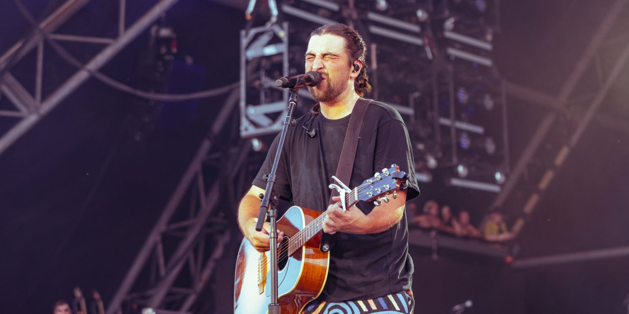 man singing into mic while holding guitar on stage